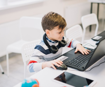 A young boy wearing headphones is focused on using a laptop, immersed in his digital experience.