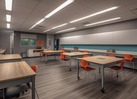 Modern classroom with empty desks, orange chairs, and fluorescent lighting.