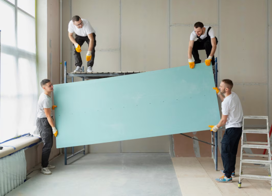 Workers carrying a large blue panel in a construction site.