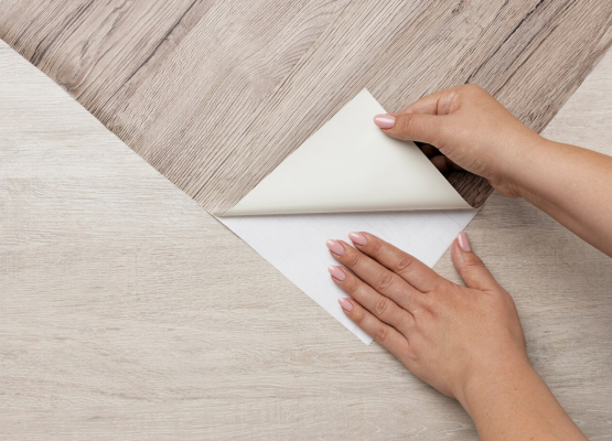 Hands applying wallpaper on a wooden surface.