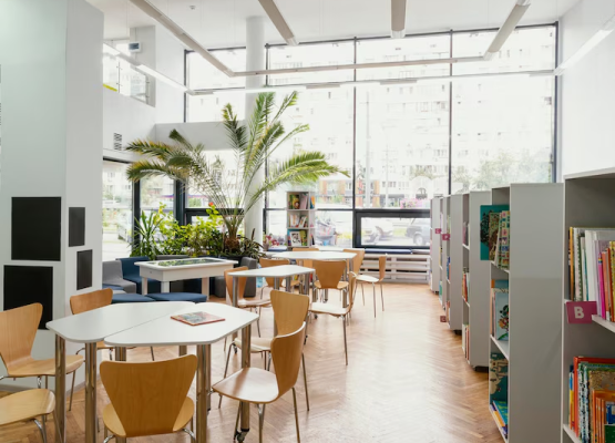 Modern library interior with bookshelves, tables, chairs, and large windows.