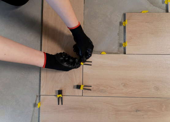 Hands in gloves laying laminate flooring with plastic spacers.