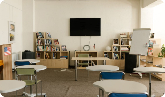 Classroom with desks, a bookshelf, TV, and whiteboard.