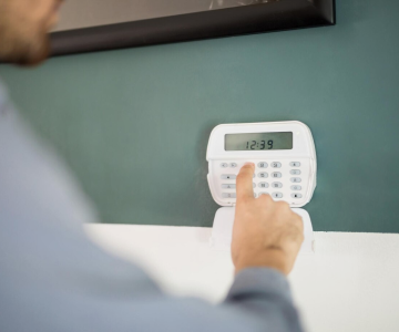 A person is entering a code on a white security system keypad mounted on a wall.