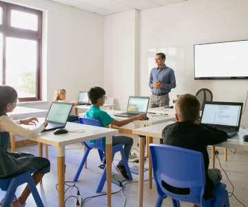 Teacher standing in front of a classroom with students working on laptops.