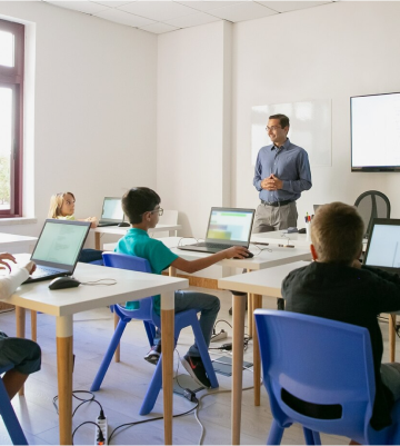 A classroom scene featuring children and adults with laptops, focusing on health and well-being education and engagement.