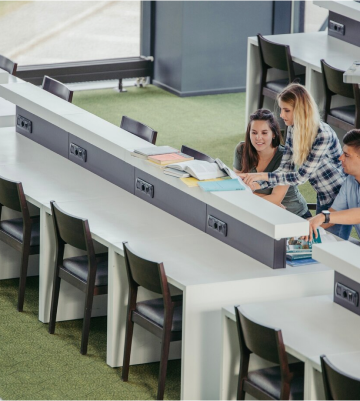 Three individuals at library tables, representing a modern approach to flexible learning and collaboration in educational spaces.