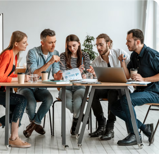 People gather around a table, focused on a laptop, symbolizing collaboration and the importance of reaching out to others.