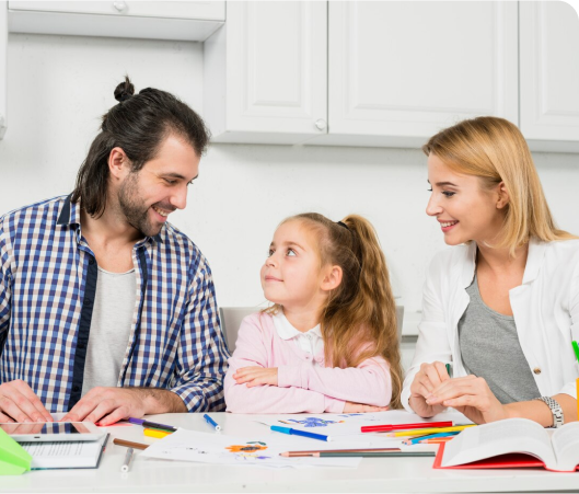 A man, woman, and a young girl sit at a table with colorful papers and markers, engaged in a cheerful conversation about values for parents.