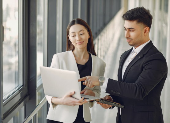 Two business individuals engaged in discussion at an office, utilizing a laptop, symbolizing management careers.