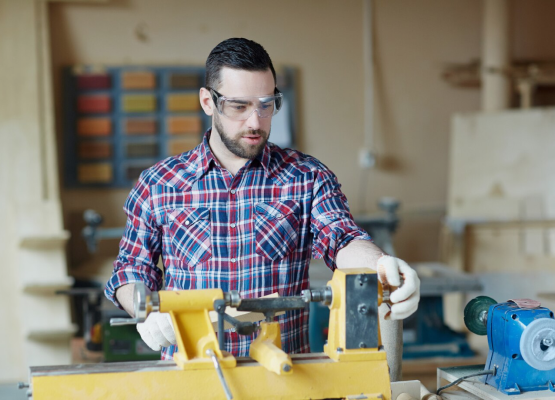 A skilled tradesman in a plaid shirt focuses on a woodworking machine, demonstrating craftsmanship and expertise.