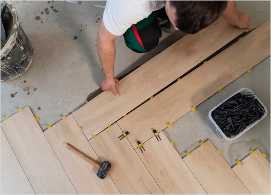 A man is engaged in the installation of wood flooring, highlighting his dedication to enhancing the interior space.