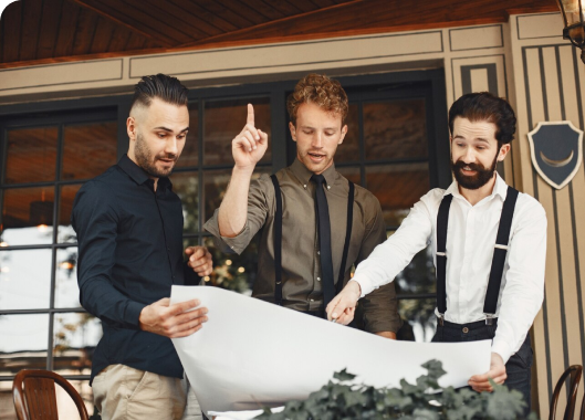 Three men standing by a table, analyzing a blueprint together, showcasing a moment of strategic planning.