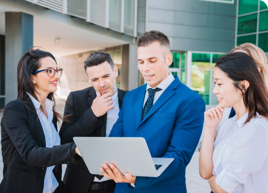 A team of business people strategizing together around a laptop in a corporate workspace.