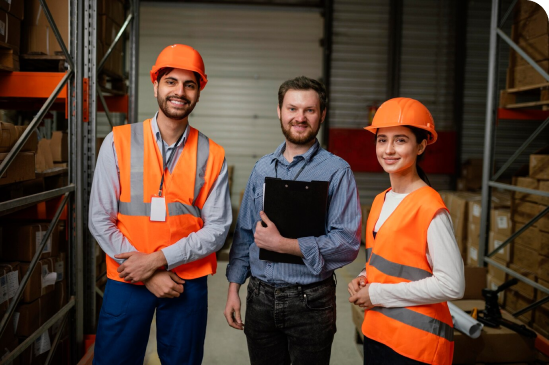 Three individuals in safety vests are positioned in a warehouse, highlighting a focus on safety and teamwork in the workspace.