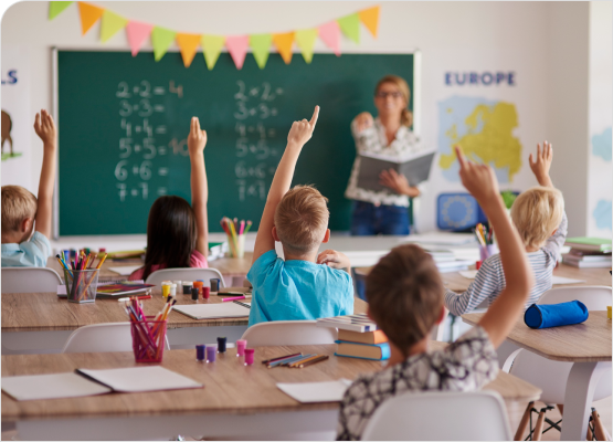 Students in a classroom enthusiastically raising their hands, eager to answer questions from the teacher.