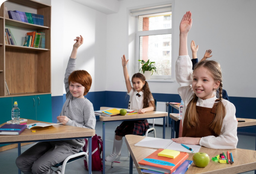 Children in a classroom eagerly raising their hands, showcasing engagement and participation in learning activities.