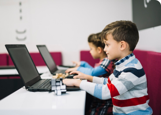 Two children engaged with laptops at a table, showcasing their interaction with technology and equipment.