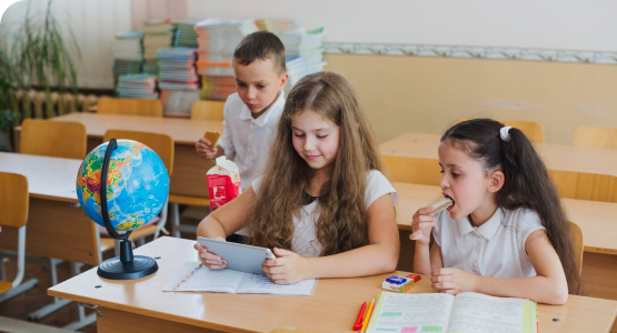 Three children sit at a desk with a globe, engaged in learning in a stable and supportive environment.