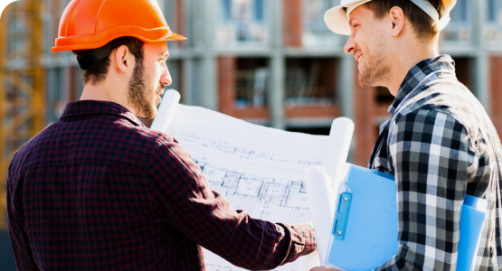 Two men wearing hard hats review construction plans together, deep in discussion at a construction site.