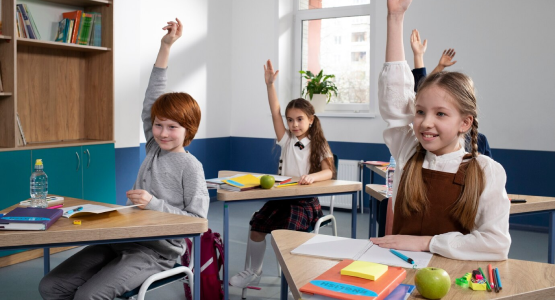 In a modular classroom, children raise their hands high, eager to share their thoughts and answers with the teacher.