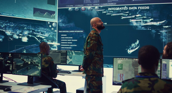 A team of soldiers examines a computer screen inside a government modular building, engaged in their work.