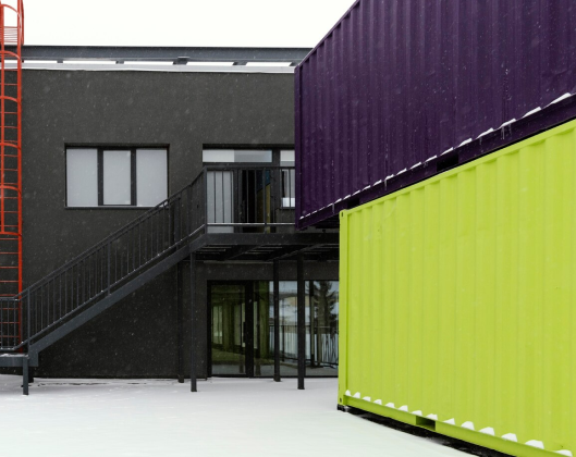 A snow-covered building surrounded by multiple shipping containers, creating a stark contrast against the winter landscape.