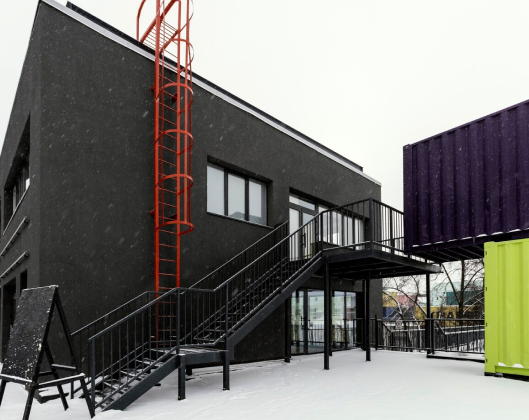 A building constructed from shipping containers, surrounded by a blanket of snow, creating a striking winter scene.