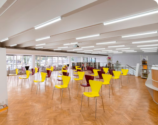 Large room filled with yellow chairs and tables, emphasizing energy efficiency in a modular space layout.