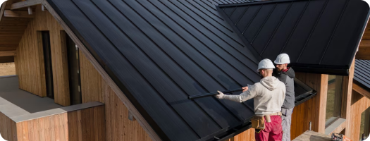 Two men installing a metal roof, focused on their work, showcasing teamwork and construction skills on a sunny day.