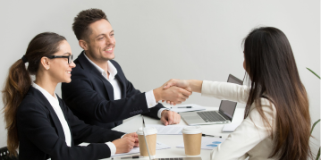 Two business professionals shaking hands across a table, symbolizing agreement and collaboration in a professional setting.