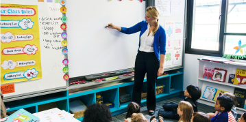 A woman teacher writing on a whiteboard, engaged in a presentation or brainstorming session, with a focus on her expression.