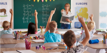 A classroom scene with children eagerly raising their hands to participate in the lesson.