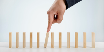 A person points at a domino board arranged with wooden blocks, illustrating a game in progress.