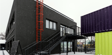 A snow-covered building surrounded by multiple shipping containers, creating a stark contrast against the white landscape.