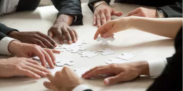 Business professionals collaborating to assemble puzzle pieces, symbolizing teamwork and problem-solving in a corporate environment.