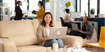 A woman seated on a couch, focused on her laptop, creating a cozy and productive home environment.