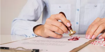 Individual signing a document featuring a red wax seal, representing formal certifications and validation of the agreement.